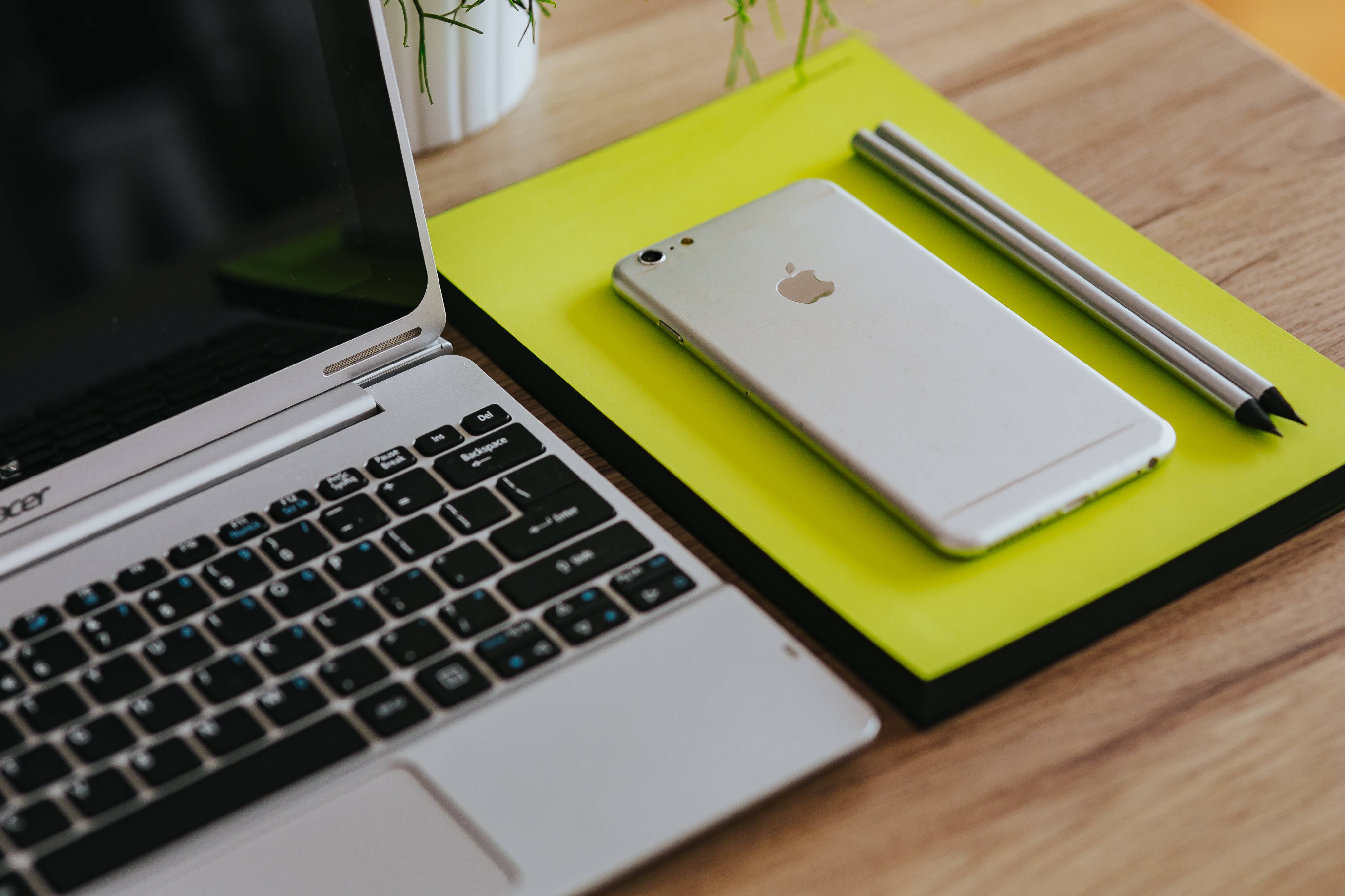 kaboompics_Silver Acer laptop, a white Apple iPhone and a yellow notebook on a wooden desk